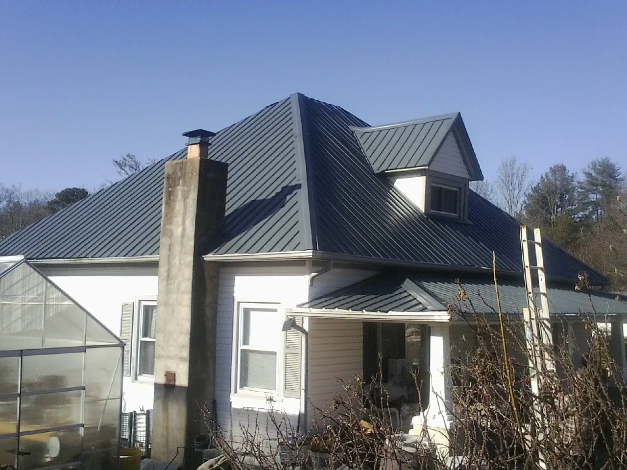 Dark blue standing seam metal roof on a white farmhouse with dormer — Slate & Tile Roof Repair by Roofing Brothers in Leverett