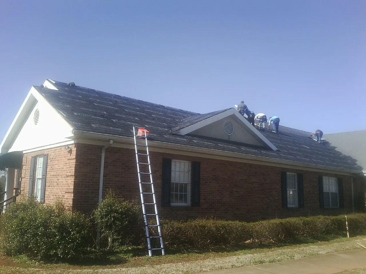 Crew tearing shingles off a brick ranch roof with a ladder set — Emergency Roof Repair work by our crew in Leverett