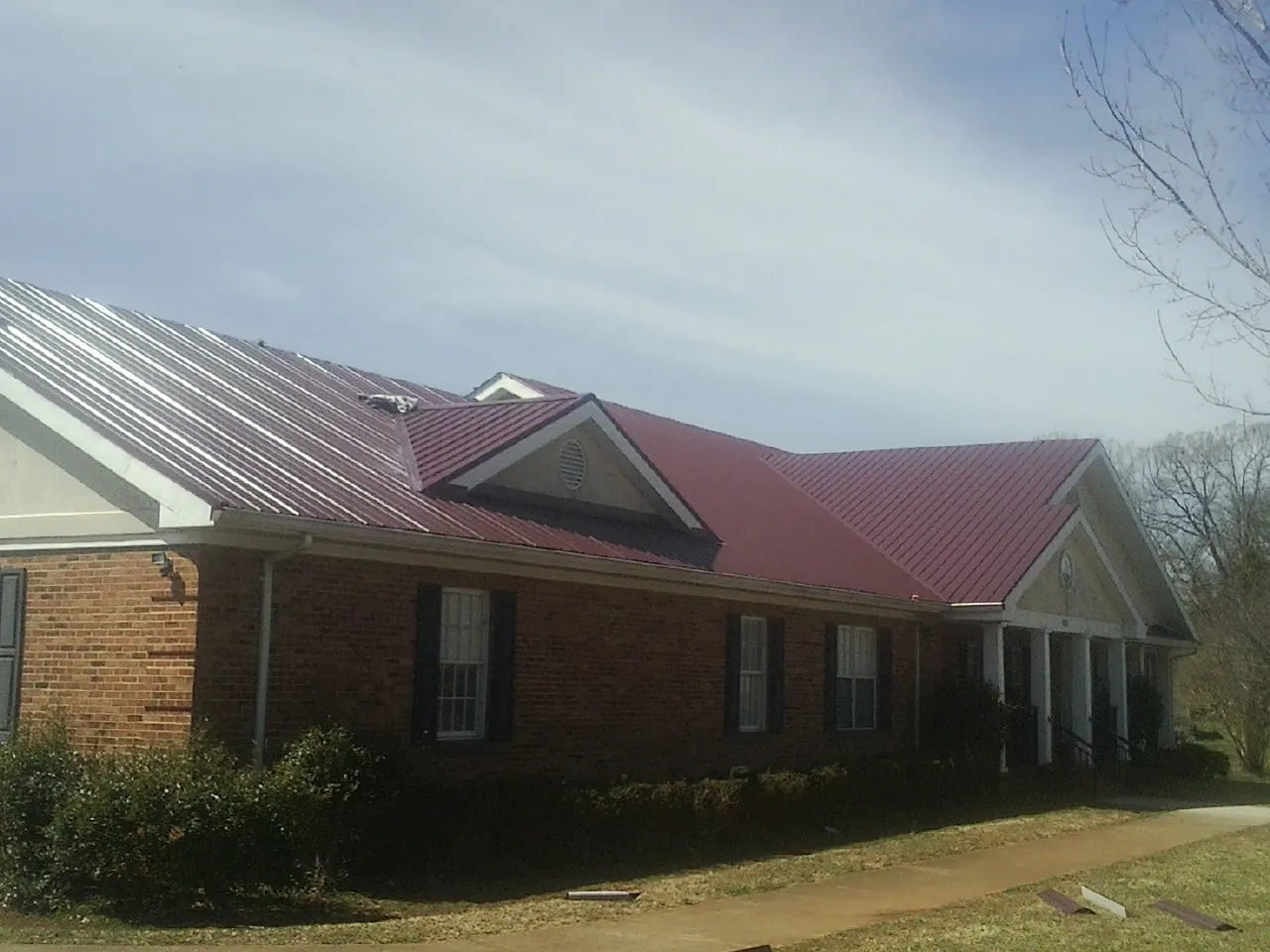 Red metal roof with gabled entries on a long brick building, from a Hail Damage Roof Repair job in Leverett