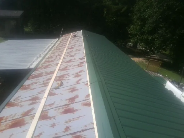 Old rusted panels beside newly installed green metal roofing — Wind Damage Roof Repair by Roofing Brothers in Leverett