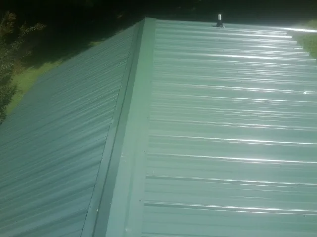New green metal panels meeting at the ridge of a roof — Flat Roof Repair work by our crew in Leverett