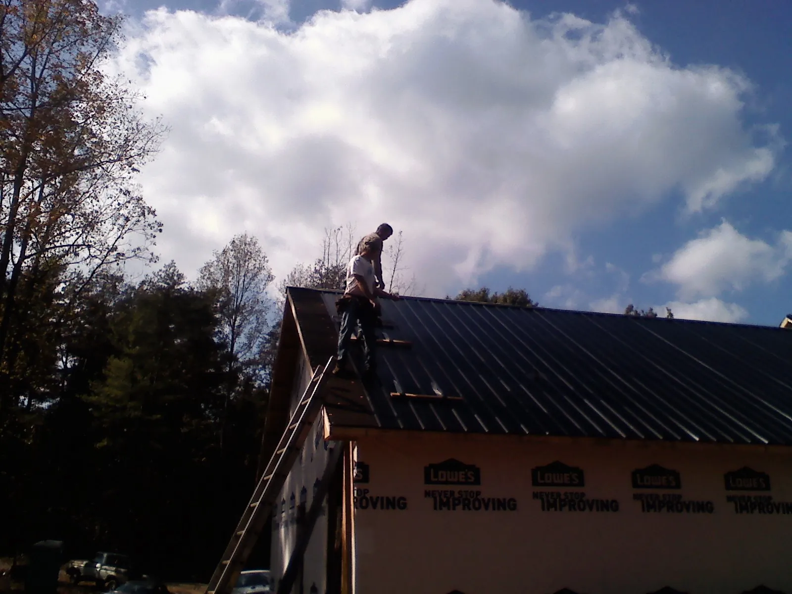 Roofer fastening dark metal panels high against a cloudy sky, from a Roof Inspection job in Leverett