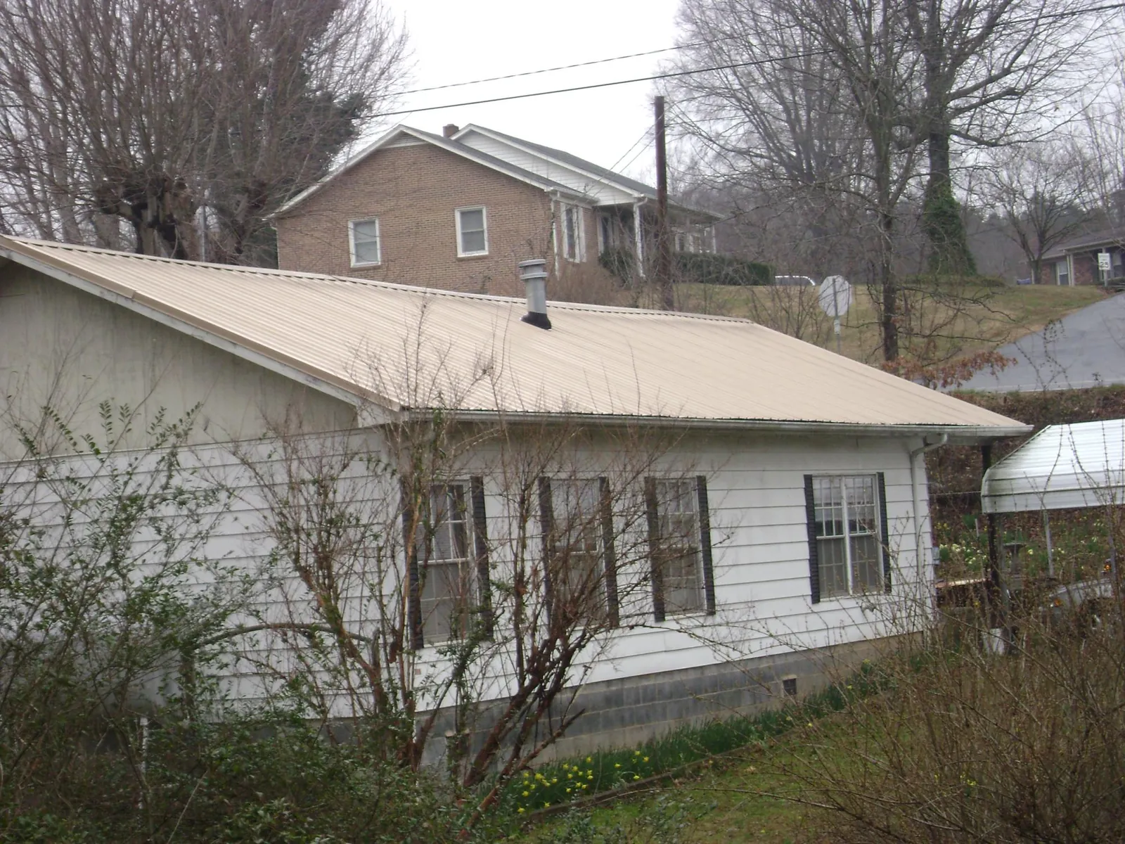 Tan metal roof on a white sided house set into a hillside — Commercial Roofing by Roofing Brothers in Leverett