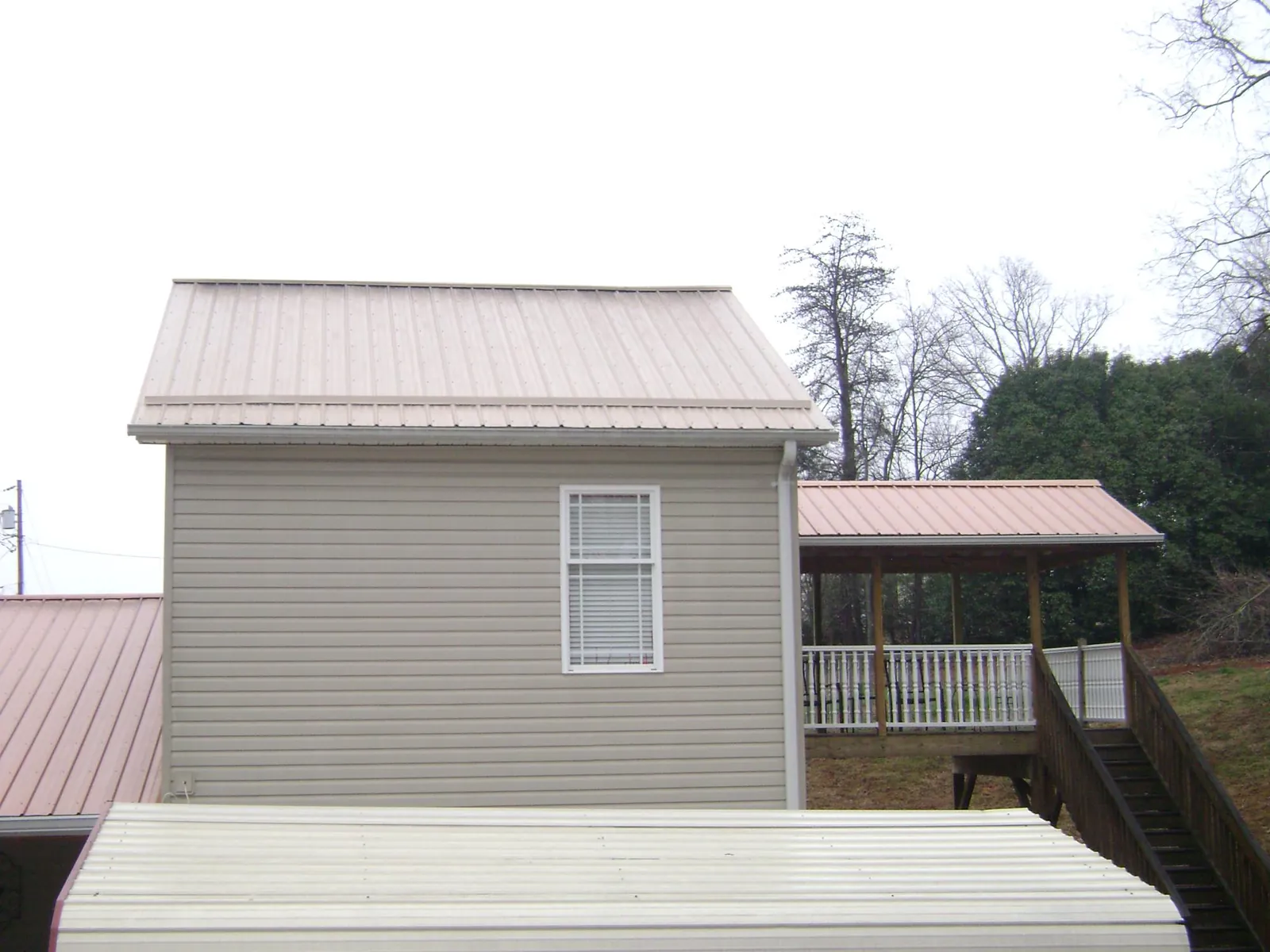 Tan metal roofs on a two story addition and attached porch, from a Roof Replacement job in Leverett